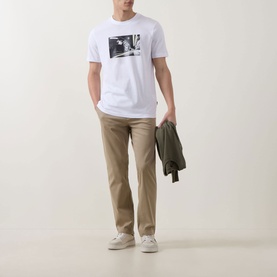Model wearing Hugo Boss Orange Te Motors Logo Graphic T-Shirt in white, styled with tan chinos, white trainers, and carrying an olive jacket.
