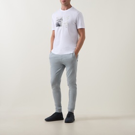 Model wearing Hugo Boss Orange Te Motors Logo Graphic T-Shirt in white with grey joggers and navy trainers.