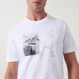 Model wearing Hugo Boss Orange Te Motors Logo Graphic T-Shirt in white, featuring a monochrome motor graphic print on the chest.