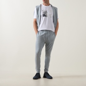 Model wearing Hugo Boss Orange Te Motors Logo Graphic T-Shirt in white, styled with grey joggers and dark navy trainers.