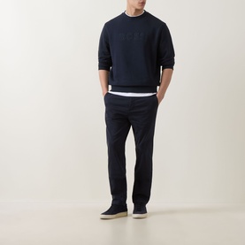 Model wearing Hugo Boss Orange dark blue cotton crew neck sweatshirt, styled with navy trousers and white underlayer.