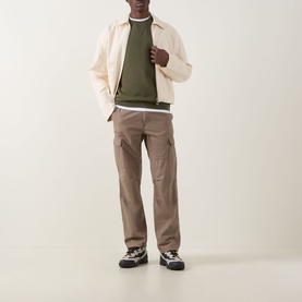 Model wearing Hugo Boss Orange Westart Logo Sweater in Bright Green, styled with cream jacket, taupe cargo trousers and chunky trainers.