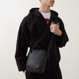 Model carrying Hugo Boss Jace Messenger Bag in black with gunmetal hardware and adjustable crossbody strap, styled with black zip-up hoodie