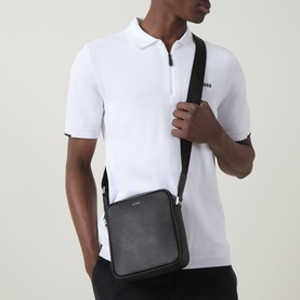Model carrying Hugo Boss Northon Zip Crossbody Bag in black with silver-tone logo, adjustable black shoulder strap, styled with white polo shirt
