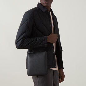 Model carrying Hugo Boss Northon Leather Crossbody Bag in black with silver-tone fittings and adjustable strap, styled with black quilted jacket