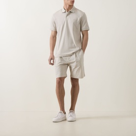 Model wearing Hugo Boss Orange light beige cotton polo shirt, styled with matching beige shorts and white trainers.