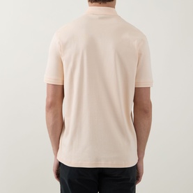 Model wearing Hugo Boss Orange polo in light pastel orange, rear view, short sleeves, 100% cotton, paired with dark trousers.