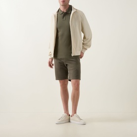 Model wearing Hugo Boss Orange Bright Green polo shirt with cream zip jacket, khaki shorts, and white trainers