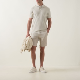 Model wearing Hugo Boss Orange Light Beige cotton polo shirt, styled with matching shorts and white trainers, holding a cream jacket.