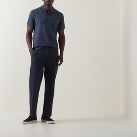 Model wearing Hugo Boss Orange Phoenix Logo Tipped Polo Shirt in dark blue, paired with navy trousers and cream trainers.