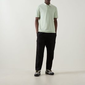Model wearing Hugo Boss Orange Phoenix Logo Polo Shirt in Open Green with black trousers and chunky trainers.