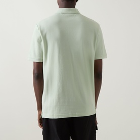 Model wearing Hugo Boss Orange Phoenix Logo Polo Shirt in Open Green, rear view, short sleeves, straight hem, styled with black trousers.