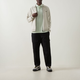 Model wearing Hugo Boss Orange Phoenix Logo Polo Shirt in Open Green, styled with cream zip jacket, black cargo trousers and chunky trainers.