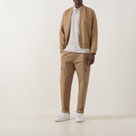 Model wearing Hugo Boss Orange Prime Logo Polo Shirt in Light Beige, styled with tan bomber jacket, matching cargo trousers and white trainers.