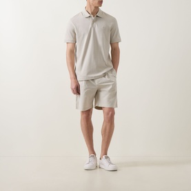 Model wearing Hugo Boss Orange light beige cotton shorts, styled with matching polo shirt and white trainers.