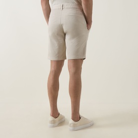 Model wearing Hugo Boss Orange light beige cotton-stretch shorts, paired with white trainers, seen from behind.