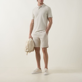 Model wearing Hugo Boss Orange light beige cotton shorts, styled with matching polo shirt, carrying cream backpack and white trainers.