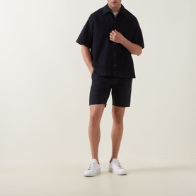 Model wearing Hugo Boss Orange dark blue cotton shorts with matching short-sleeve shirt and white trainers.