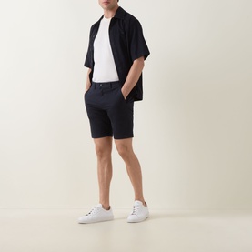 Model wearing Hugo Boss Orange dark blue cotton shorts with white T-shirt, navy open shirt, and white trainers.