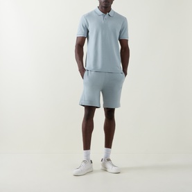 Model wearing Hugo Boss Orange Open Grey cotton shorts, styled with matching polo shirt and white trainers.