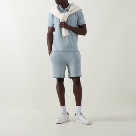 Model wearing Hugo Boss Orange Open Grey cotton shorts, styled with matching tee and white trainers, cream sweater draped over shoulders