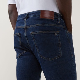 Model wearing Hugo Boss Orange Delaware Slim Fit Jeans in navy, showing rear patch pockets and brown leather logo patch detail.