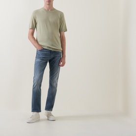 Model wearing Hugo Boss Orange Delaware Mid-Rise Slim Leg Jeans in medium grey, styled with a sage green T-shirt and white trainers.