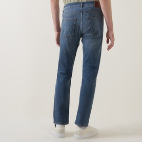 Model wearing Hugo Boss Orange Delaware Mid-Rise Slim Leg Jeans in medium grey, rear view, styled with white trainers and brown belt.