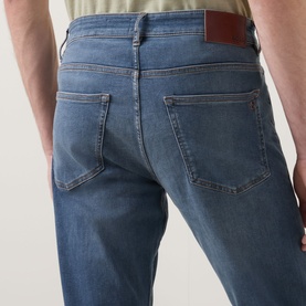 Model wearing Hugo Boss Orange Delaware Mid-Rise Slim Leg Jeans in medium grey, showing rear five-pocket detail and brown leather patch.