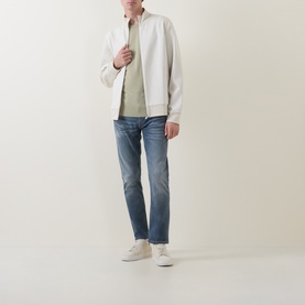 Model wearing Hugo Boss Orange Delaware Mid-Rise Slim Leg Jeans in medium grey, styled with white zip jacket and cream trainers.