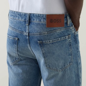 Model wearing Hugo Boss Orange straight jeans in turquoise/aqua denim, close-up of back pockets with tan leather BOSS logo patch