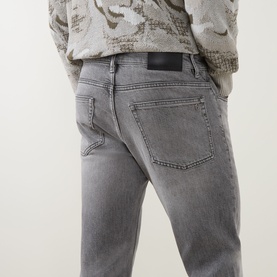Model wearing Hugo Boss Orange Remained Straight Leg Jeans in light grey with faded detailing, styled with a patterned sweatshirt.