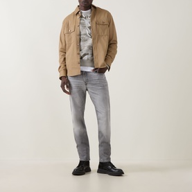 Model wearing Hugo Boss Orange Remained Straight Leg Jeans in light grey with faded detailing, styled with a tan overshirt and black boots.