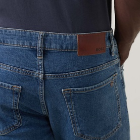 Model wearing Hugo Boss Orange bright blue straight jeans, close-up of back pockets with brown leather logo patch detail.