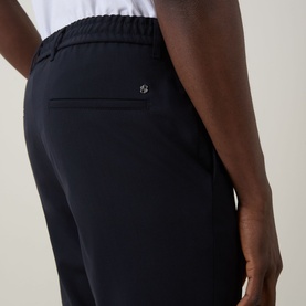 Model wearing Hugo Boss dark blue trousers, close-up of rear pocket with logo detail, elasticated waistband, wool-blend fabric