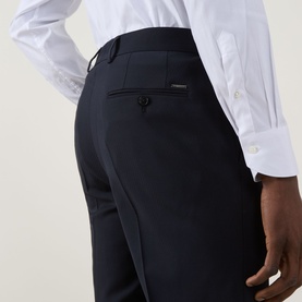 Model wearing Hugo Boss George Slim-Leg Trousers in dark blue, showing rear pockets with button fastenings and logo detail, styled with white shirt.