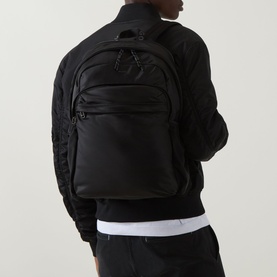 Model carrying Hugo Ayden Backpack in black, worn on back, featuring logo carry loop and front zip pockets, styled with black bomber jacket