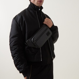 Model carrying Hugo Ethon 2.0HI Bum Bag in black, worn crossbody, with zip pockets and tonal hardware, styled with black padded jacket