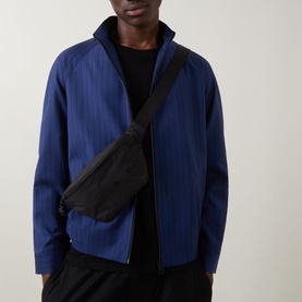 Model carrying Hugo REHX Logo Belt Bag in black, worn crossbody over a blue zip-up jacket and black trousers.