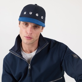 Model with Hugo Moonstruck Logo Cap in Open Blue, curved visor, contrasting panels, embroidered logo, styled with navy zip-up jacket