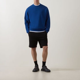 Model wearing Hugo Open Blue cotton crew neck sweatshirt with black shorts, black socks and dark trainers.