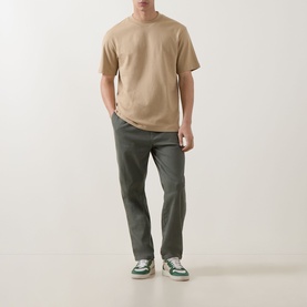 Model wearing Hugo medium beige cotton crew neck T-shirt, styled with olive trousers and green and white trainers.