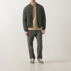 Model wearing Hugo Medium Beige cotton crew neck T-shirt, styled with olive quilted bomber jacket, grey trousers and green trainers.