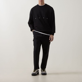 Model wearing Hugo black cotton crew neck sweatshirt with chest pockets, styled with black trousers and chunky lace-up shoes.