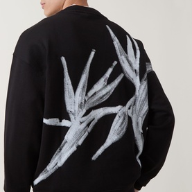Model wearing Hugo black cotton crew neck sweatshirt, back view showing large white botanical graphic print across shoulders.