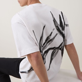Model wearing Hugo Crew Neck T in Natural white, back view showing bold black botanical brushstroke print, styled with black trousers.