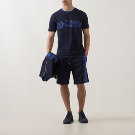Model wearing Hugo dark blue cotton crew neck T-shirt with graphic print, styled with navy shorts, carrying a jacket, wearing navy trainers.