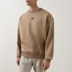 Model wearing Hugo beige crew neck sweatshirt with small logo patch, styled with light grey trousers.