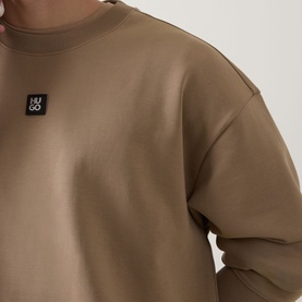 Model wearing Hugo crew neck sweatshirt in beige with small black logo patch at chest
