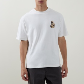 Model wearing Hugo Detzi Logo T-Shirt in Natural white, crew neck, short sleeves, small chest graphic, paired with dark trousers.